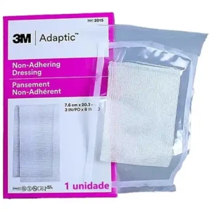 Foto em plano frontal sobre fundo branco exibindo um sachê individual do curativo malha não aderente Adaptic da 3M. À esquerda, a embalagem de papel traz uma identidade visual marcante em rosa choque e branco, destacando o logotipo preto da 3M Adaptic, as inscrições "Non-Adhering Dressing" e "Pansement Non-Adhérent", as dimensões de 7,6 cm x 20,3 cm e a frase informativa "1 unidade" na base. À direita, sobreposta à embalagem, aparece uma aba plástica transparente aberta que revela a malha de acetato de celulose esbranquiçada e porosa impregnada com petrolato.