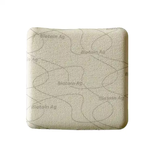Vista superior de um curativo quadrado Biatain Ag Não Adesivo de 10x10 cm, apresentando uma superfície de espuma hidrofílica macia na cor bege claro com textura porosa e linhas orgânicas escuras onduladas impressas junto à inscrição repetida da marca Biatain Ag. O dispositivo médico possui cantos arredondados e acabamento estéril, exibido de forma centralizada sobre um fundo branco minimalista.