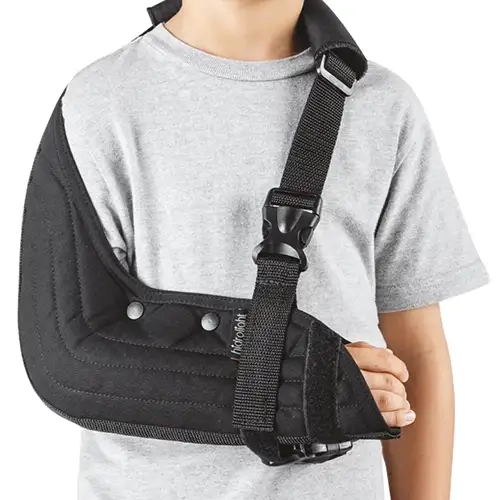 Foto em plano médio detalhado sob fundo branco isolado exibindo uma criança vestindo uma camiseta cinza mescla que utiliza o modelo Tipoia Estofada Imobilizadora Velpeau Infantil.webp no braço direito. O dispositivo ortopédico na cor preta envolve firmemente o cotovelo e o antebraço em uma bolsa de tecido estofada e acolchoada com costuras horizontais paralelas em relevo. Uma aba de tecido estende-se para cima cobrindo a articulação do ombro direito, apresentando dois botões de pressão metálicos cinzas e uma pequena etiqueta vertical preta com o logotipo da marca Hidrolight costurada na borda superior do antebraço. O sistema de sustentação é composto por uma alça de fita trançada preta com almofada protetora estofada sobre o ombro esquerdo, equipada com passador retangular metálico e uma fivela de engate rápido de poliamida preta conectada verticalmente para manter o punho estabilizado.
