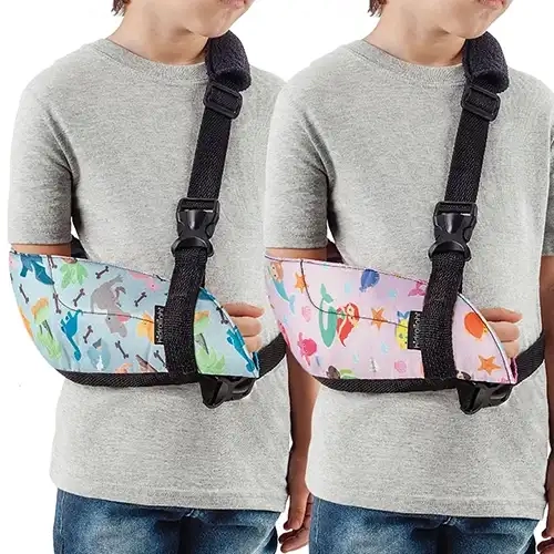 Foto em plano médio detalhado sob fundo branco isolado exibindo duas crianças lado a lado vestindo camisetas cinzas que utilizam o modelo Tipoia Imobilizadora Infantil.webp no braço direito. À esquerda, a tipoia apresenta um tecido de fundo azul-claro estampado com dinossauros coloridos e ossos, envolvendo o cotovelo e o antebraço com acabamento em viés preto. À direita, a outra tipoia exibe uma estampa de fundo rosa com temática de sereias, peixes e estrelas-do-mar. Ambos os modelos trazem uma pequena etiqueta vertical preta com a marca Hidrolight costurada na frente e contam com uma alça de fita trançada preta que passa pelo ombro esquerdo, equipada com almofada protetora estofada, passador de regulagem e fivela de engate rápido preta conectada verticalmente, além de uma tira estabilizadora horizontal preta ajustável ao redor da cintura.