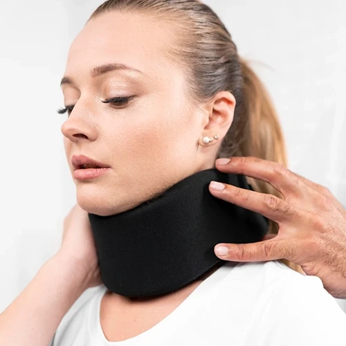 Mulher utilizando colar cervical ortopédico de espuma cinza com design anatômico e fecho ajustável. O equipamento oferece suporte estável para a coluna, auxiliando na imobilização leve e alívio de tensões no pescoço.